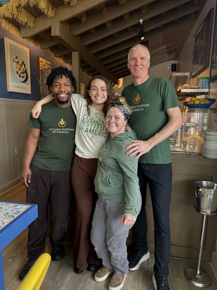 Four smiling people in Culinary Institute of America shirts gathered inside the Oyster Bar.